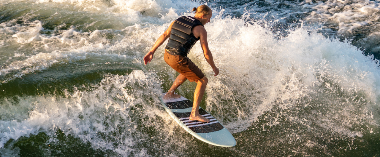 man wakesurfing behind red WTSurf wake boat